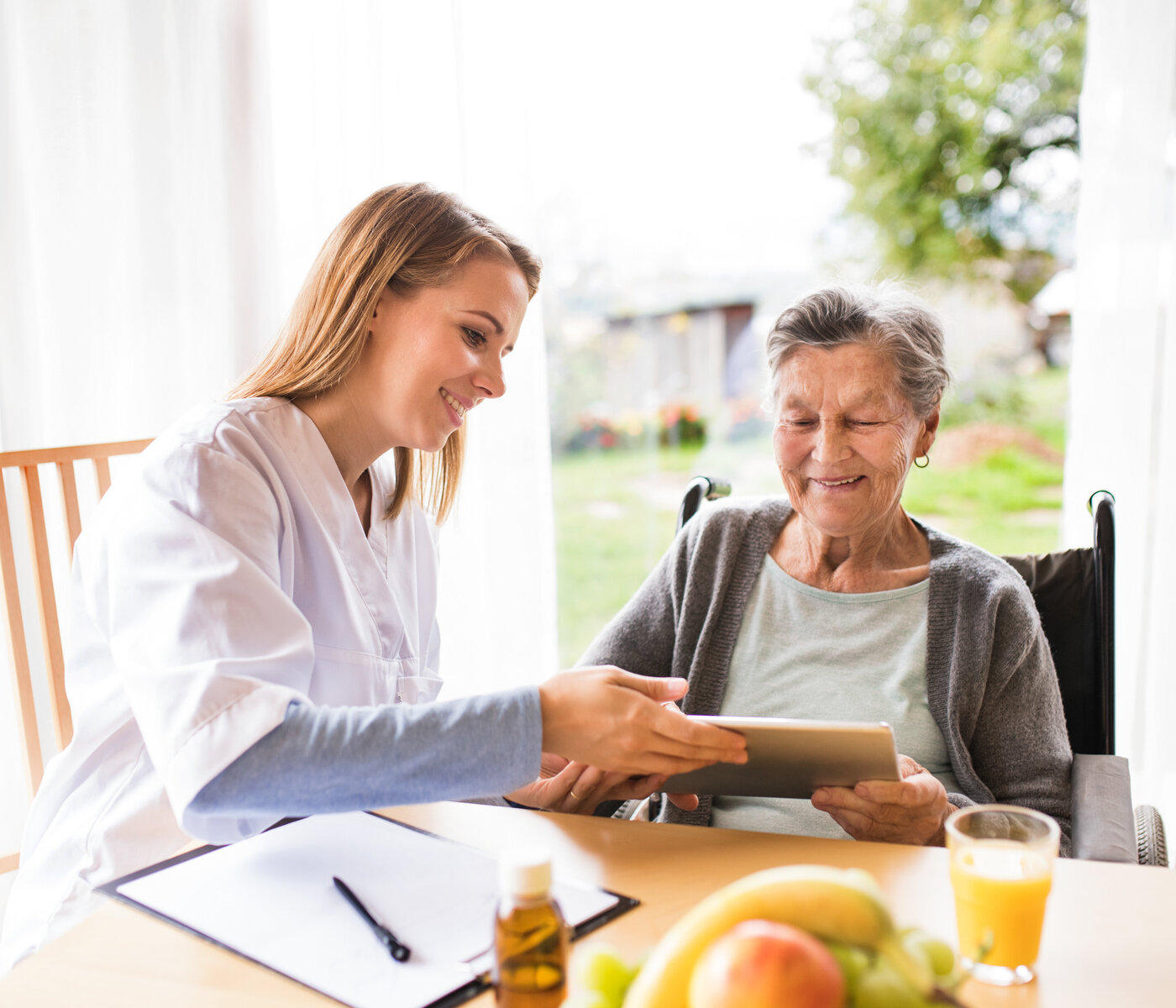 Pflegefachperson reicht einer älteren Patientin einen Tablet